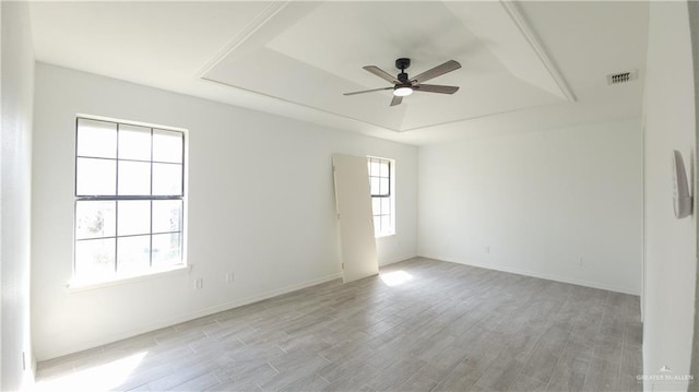 unfurnished room with visible vents, baseboards, ceiling fan, a tray ceiling, and light wood-type flooring