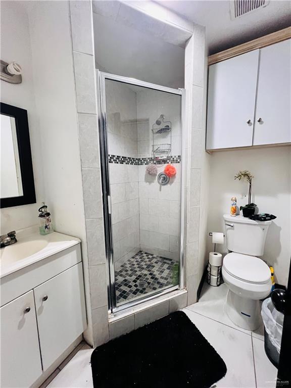 bathroom with vanity, a shower with shower door, tile patterned floors, and toilet