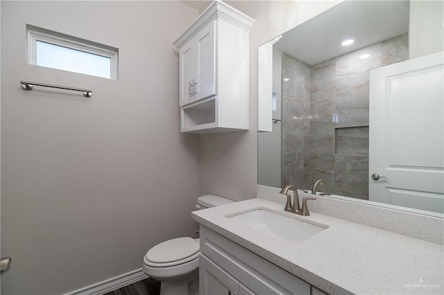 full bath with toilet, baseboards, tiled shower, and vanity