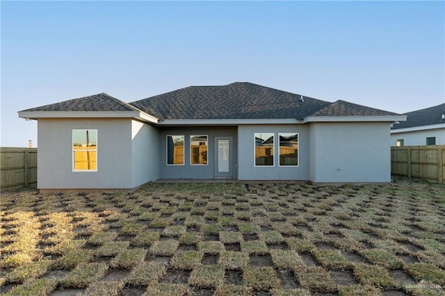 rear view of house featuring a shingled roof, fence private yard, and stucco siding