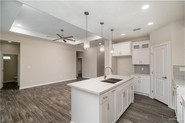 kitchen with dark wood-style floors, a tray ceiling, a sink, and decorative backsplash