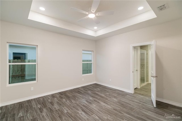 empty room featuring recessed lighting, a raised ceiling, baseboards, and wood finished floors