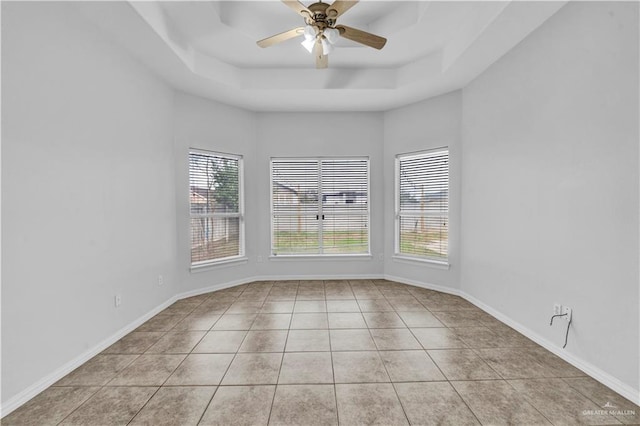 tiled spare room featuring a raised ceiling and ceiling fan