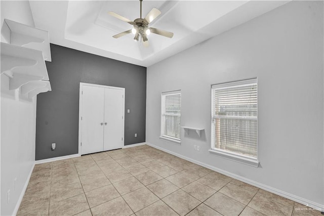 empty room featuring a raised ceiling, light tile patterned floors, and ceiling fan