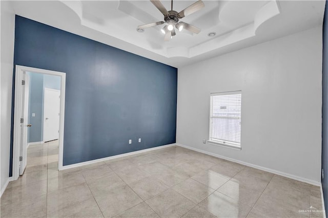 empty room with light tile patterned floors, a tray ceiling, and ceiling fan