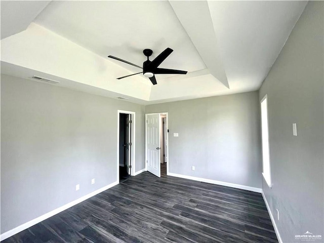 empty room with baseboards, visible vents, a ceiling fan, a raised ceiling, and dark wood-style flooring