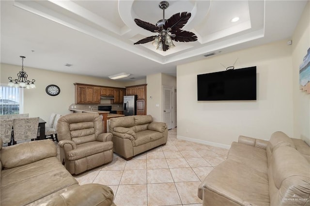 living room featuring ceiling fan with notable chandelier, a raised ceiling, and light tile patterned flooring