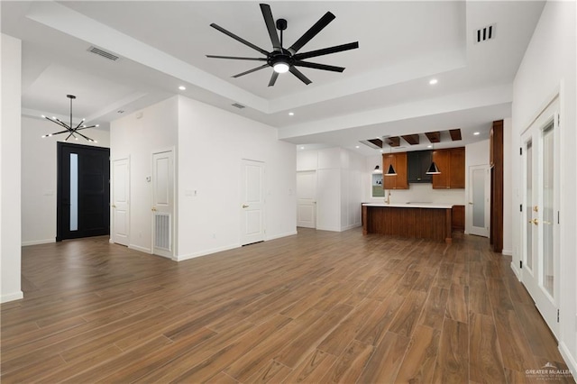 unfurnished living room with dark hardwood / wood-style flooring, ceiling fan with notable chandelier, and a tray ceiling