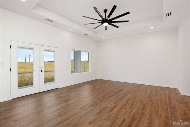 empty room featuring french doors, dark hardwood / wood-style flooring, a tray ceiling, and ceiling fan