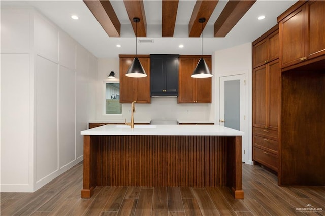 kitchen with a center island with sink, decorative light fixtures, beam ceiling, and sink