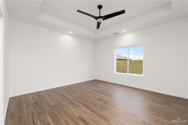 unfurnished room featuring ceiling fan, dark hardwood / wood-style flooring, and a tray ceiling