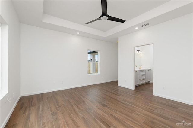 unfurnished bedroom with ensuite bathroom, a raised ceiling, ceiling fan, and dark hardwood / wood-style floors