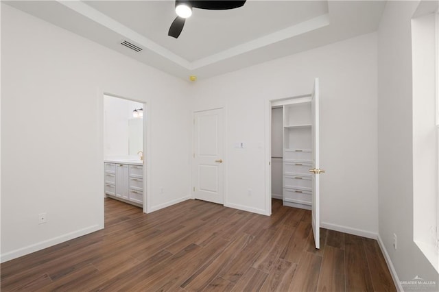 unfurnished bedroom featuring a tray ceiling, connected bathroom, ceiling fan, and dark hardwood / wood-style floors