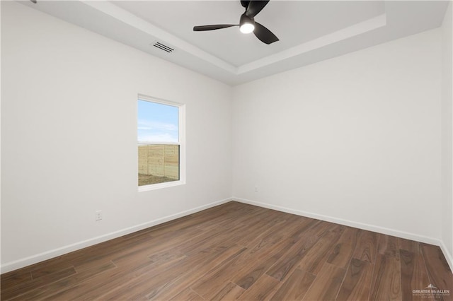 empty room featuring ceiling fan, dark wood-type flooring, and a tray ceiling