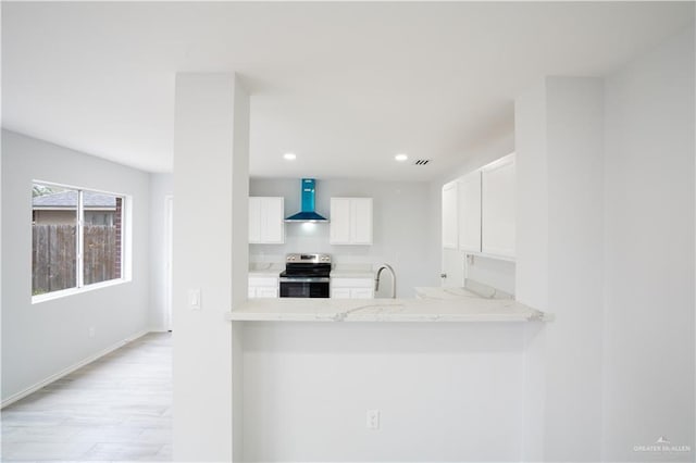 kitchen featuring stainless steel range with electric stovetop, white cabinets, wall chimney range hood, light stone countertops, and kitchen peninsula