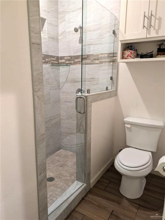 bathroom with hardwood / wood-style floors, a shower with door, and toilet