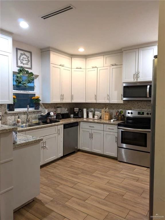 kitchen featuring light stone countertops, appliances with stainless steel finishes, light wood-type flooring, tasteful backsplash, and white cabinetry