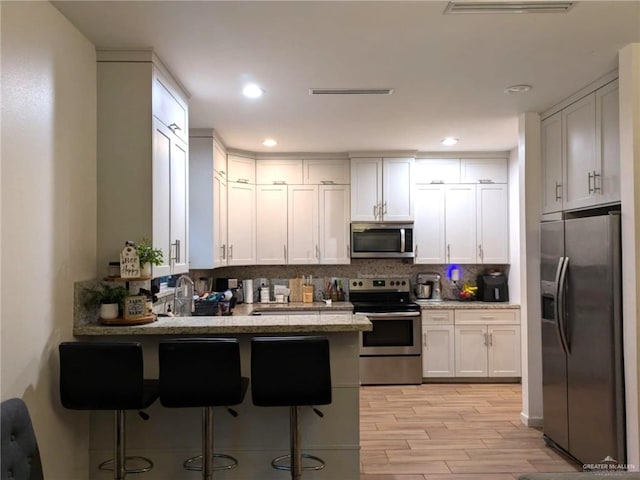 kitchen featuring a kitchen bar, appliances with stainless steel finishes, decorative backsplash, light hardwood / wood-style flooring, and white cabinetry