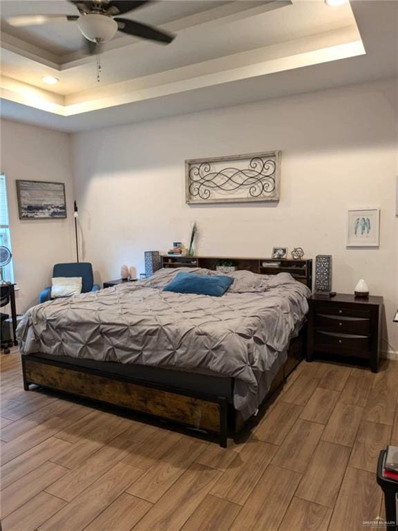 bedroom with hardwood / wood-style floors, a tray ceiling, and ceiling fan