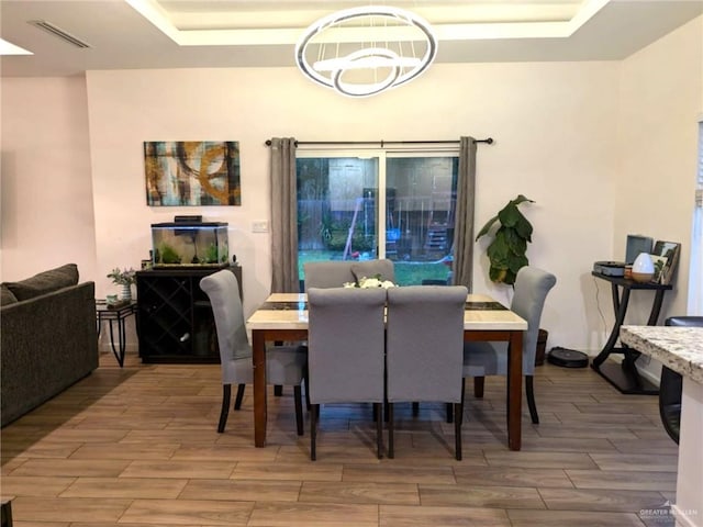 dining area with hardwood / wood-style floors, an inviting chandelier, and a raised ceiling