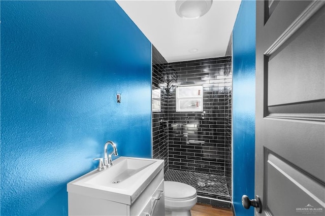 bathroom with vanity, a textured wall, wood finished floors, toilet, and a stall shower