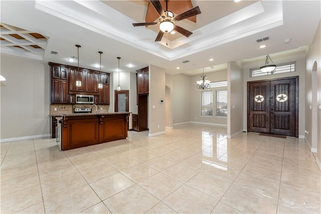 kitchen with a kitchen island with sink, backsplash, pendant lighting, and light stone countertops