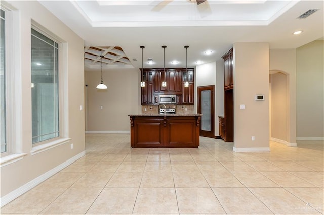 kitchen with dark stone counters, hanging light fixtures, coffered ceiling, light tile patterned floors, and a center island with sink