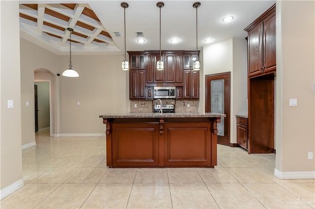 kitchen featuring appliances with stainless steel finishes, a kitchen island with sink, hanging light fixtures, coffered ceiling, and light stone countertops