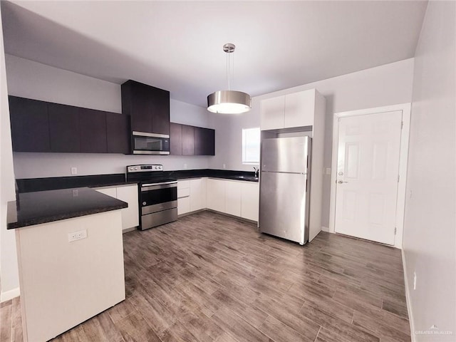 kitchen featuring stainless steel appliances, sink, decorative light fixtures, white cabinetry, and light hardwood / wood-style flooring