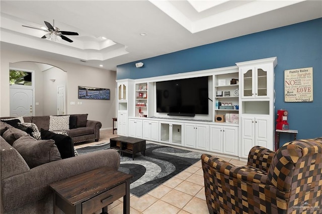 living room with built in shelves, a raised ceiling, ceiling fan, and light tile patterned flooring