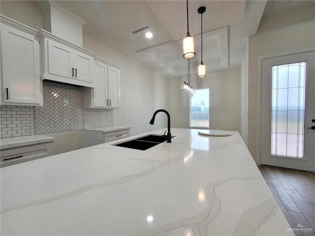 kitchen featuring white cabinetry, light stone countertops, sink, hanging light fixtures, and tasteful backsplash