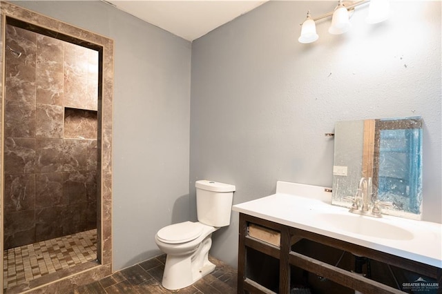 bathroom with a tile shower, vanity, and toilet