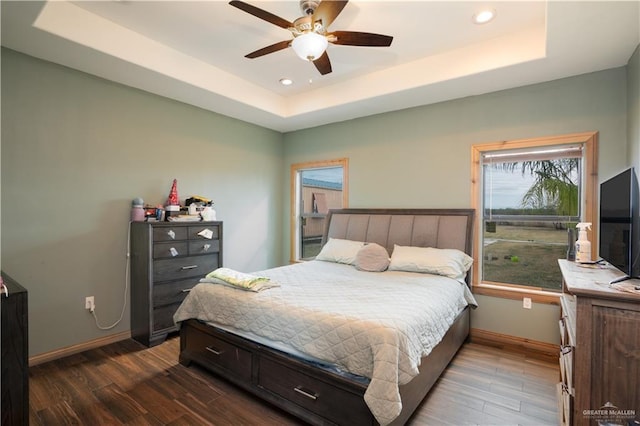 bedroom with recessed lighting, a raised ceiling, dark wood finished floors, and baseboards