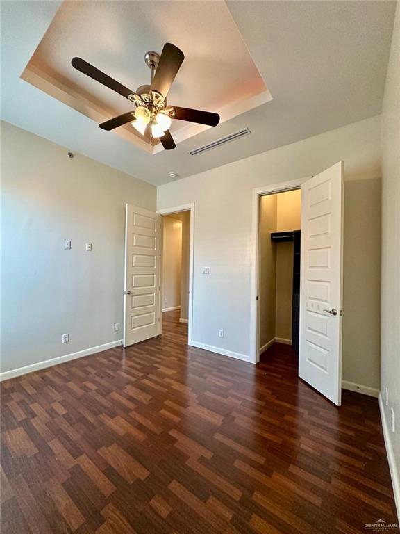 unfurnished bedroom with a spacious closet, a raised ceiling, ceiling fan, and dark wood-type flooring