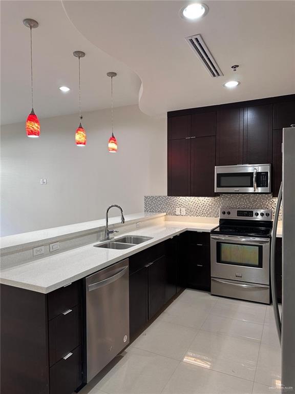 kitchen with sink, backsplash, pendant lighting, light tile patterned floors, and appliances with stainless steel finishes