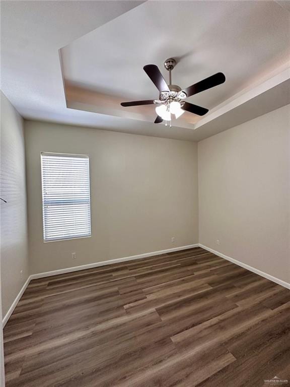 unfurnished room featuring ceiling fan, dark hardwood / wood-style flooring, and a tray ceiling