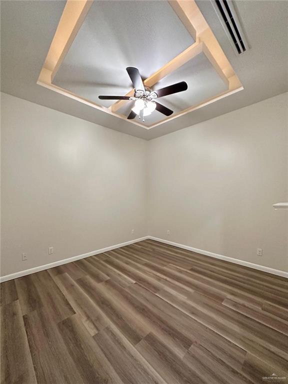 unfurnished room featuring dark hardwood / wood-style floors, ceiling fan, and a tray ceiling