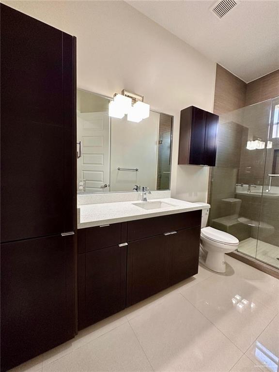 bathroom featuring toilet, vanity, tile patterned floors, and an enclosed shower