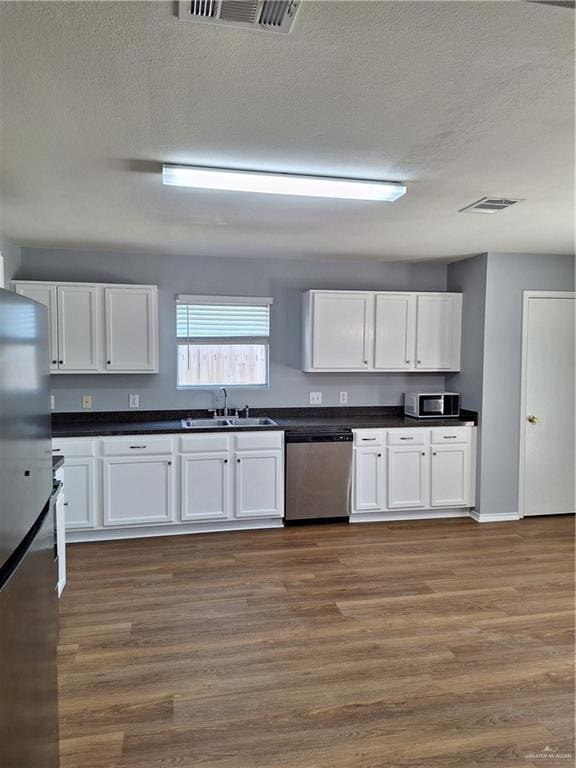 kitchen with white cabinetry, sink, stainless steel appliances, dark hardwood / wood-style floors, and a textured ceiling