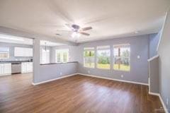 unfurnished living room with ceiling fan, a healthy amount of sunlight, and dark wood-type flooring