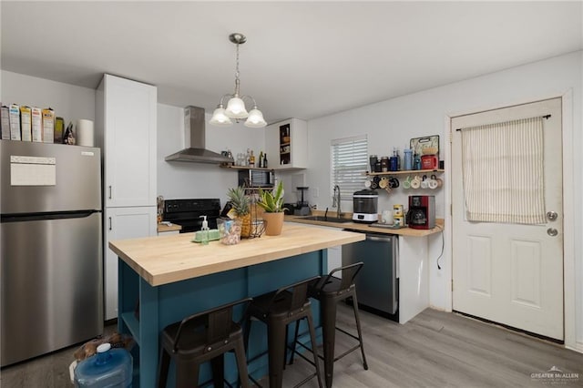 kitchen with wall chimney exhaust hood, a kitchen bar, wooden counters, hanging light fixtures, and stainless steel appliances