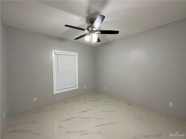 empty room with a ceiling fan, marble finish floor, and baseboards