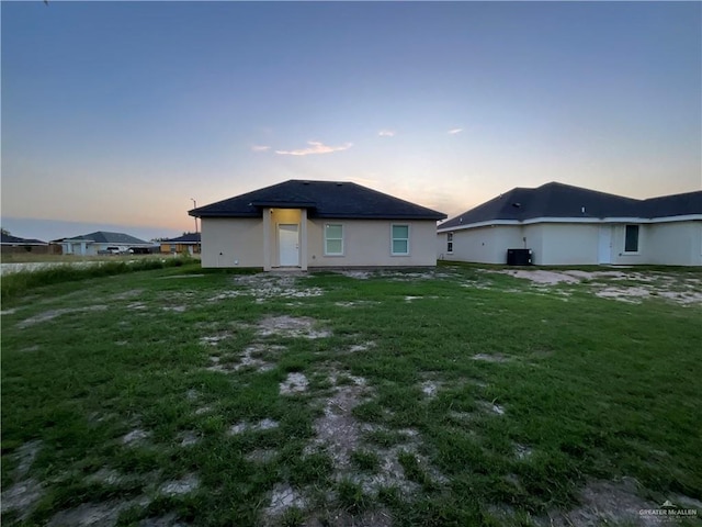 back of property with a lawn, stucco siding, and central air condition unit