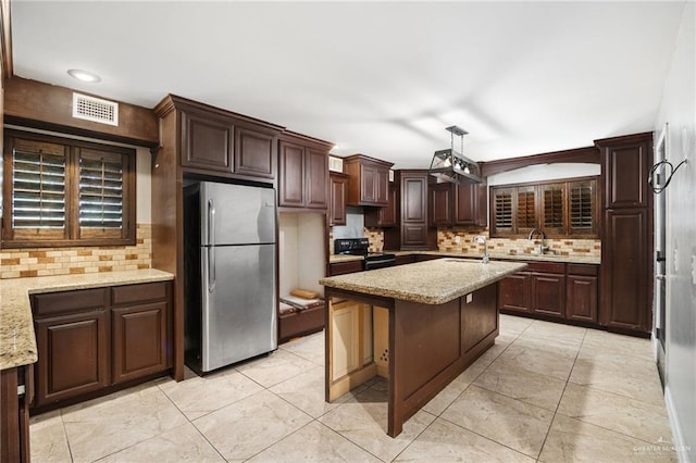 kitchen featuring stainless steel refrigerator, light stone countertops, black range with electric stovetop, decorative backsplash, and a kitchen island