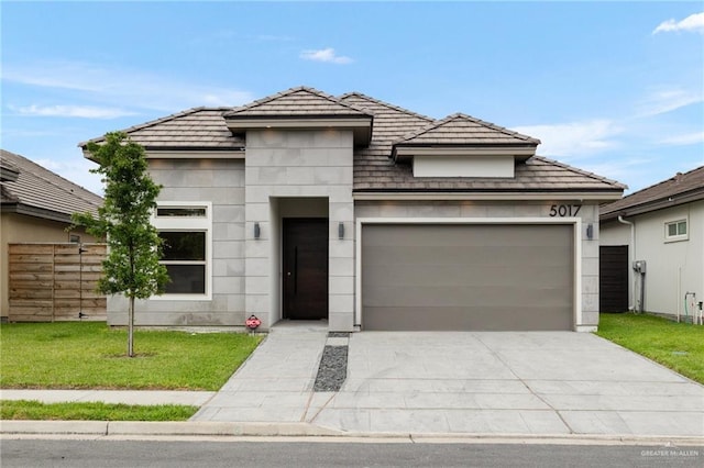 prairie-style home featuring concrete driveway, fence, a front yard, and a garage