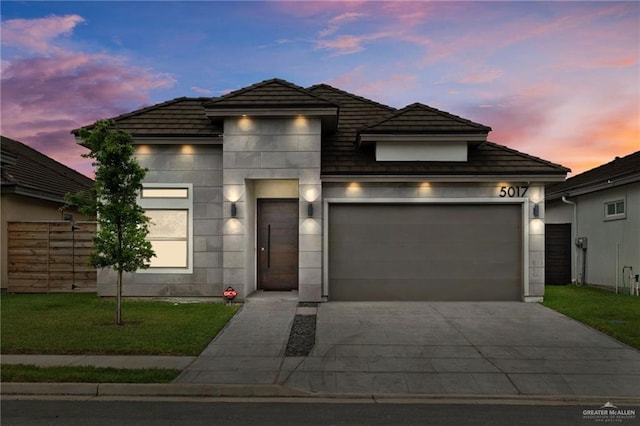 prairie-style home featuring a tile roof, a front lawn, concrete driveway, a garage, and stucco siding
