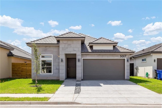 prairie-style home featuring a tile roof, a front lawn, concrete driveway, fence, and an attached garage