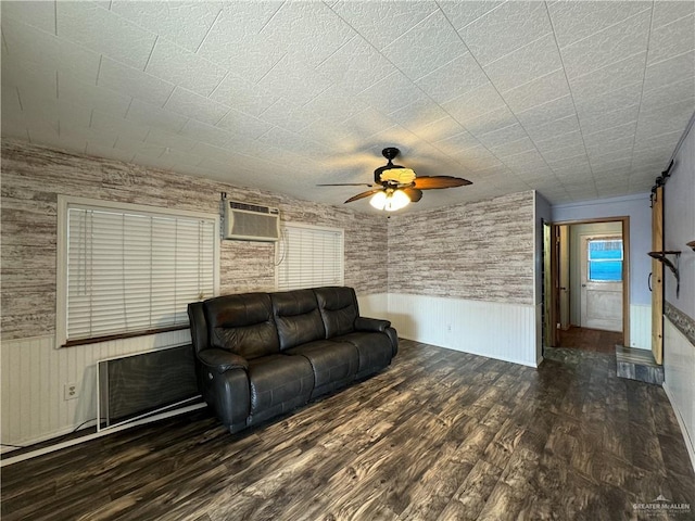 unfurnished living room with a wainscoted wall, a ceiling fan, a wall unit AC, and wood finished floors