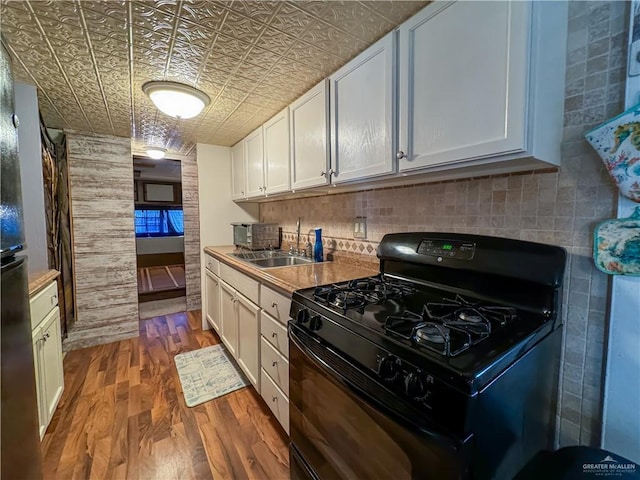 kitchen featuring black range with gas stovetop, decorative backsplash, wood finished floors, an ornate ceiling, and a sink