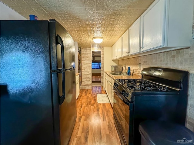 kitchen featuring black appliances, light wood-style flooring, a sink, an ornate ceiling, and white cabinets